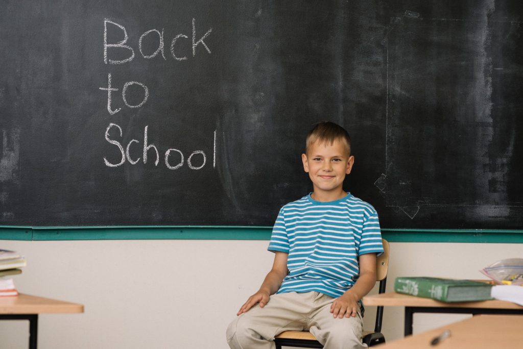 Uczeń siedzi na krześle tyłem do tablicy. Na tablicy jest napis "Back to School".